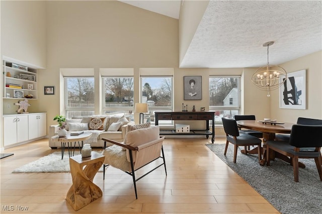 living area featuring a textured ceiling, a high ceiling, an inviting chandelier, and light wood-style floors