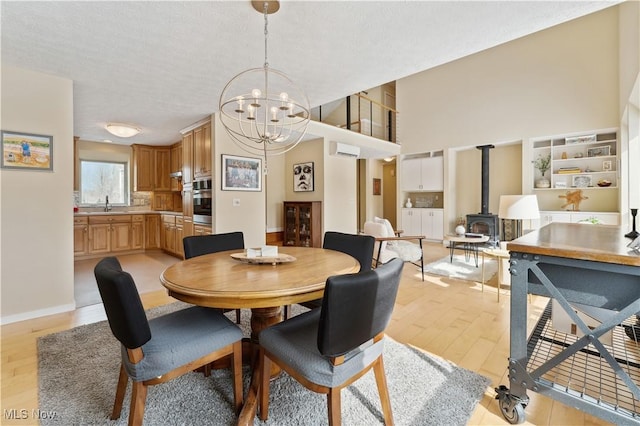 dining area featuring a chandelier, a textured ceiling, baseboards, light wood finished floors, and a wood stove