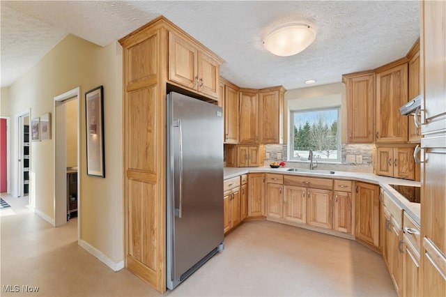 kitchen featuring light countertops, a sink, backsplash, and stainless steel refrigerator