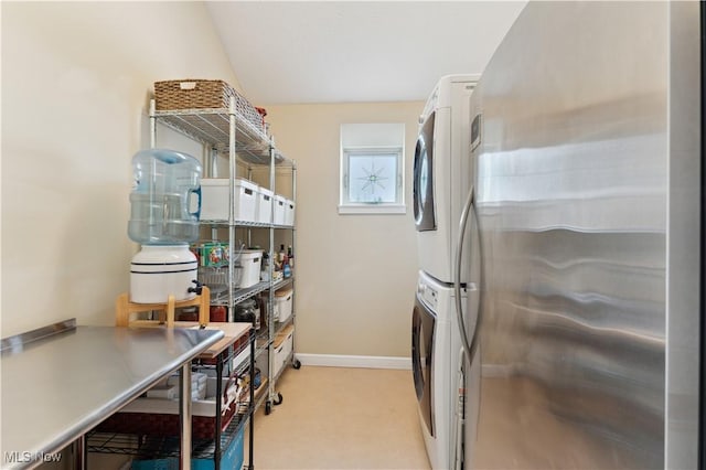 kitchen with stacked washing maching and dryer, baseboards, light colored carpet, and freestanding refrigerator