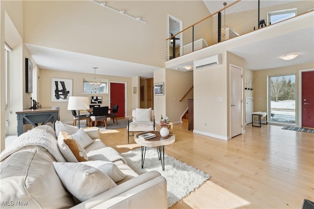 living room with stairway, an inviting chandelier, a high ceiling, light wood-type flooring, and a wall mounted AC