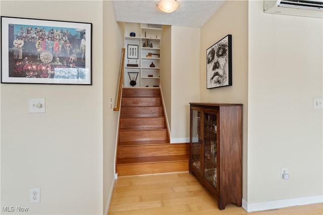 interior space with light wood finished floors, baseboards, a wall unit AC, stairs, and a textured ceiling