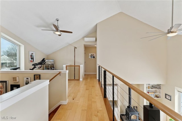 corridor with vaulted ceiling, an AC wall unit, light wood-style flooring, and an upstairs landing