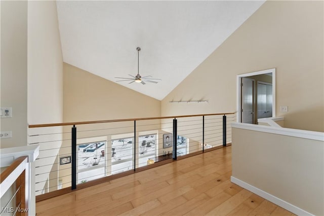 hallway with high vaulted ceiling, light wood finished floors, an upstairs landing, and baseboards