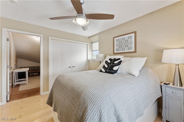 bedroom with a textured ceiling, lofted ceiling, light wood-style flooring, a ceiling fan, and a closet