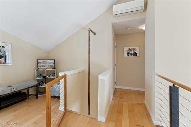 corridor featuring vaulted ceiling, light wood finished floors, a wall mounted AC, and an upstairs landing