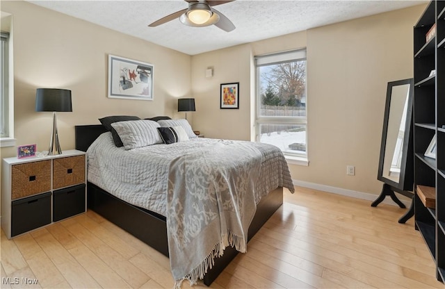 bedroom featuring light wood-style floors, a textured ceiling, baseboards, and a ceiling fan