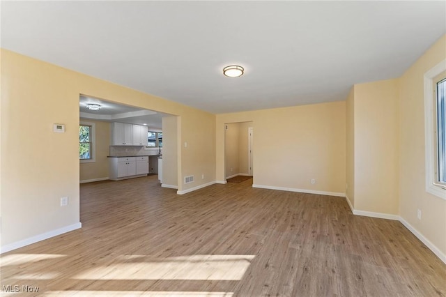 unfurnished living room featuring baseboards, visible vents, and light wood-style floors