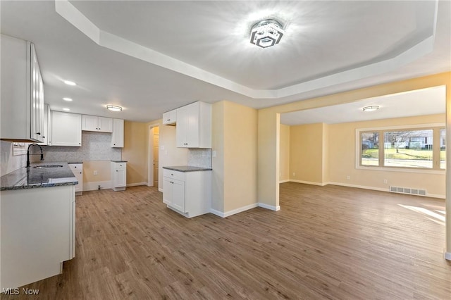 kitchen with wood finished floors, a sink, visible vents, open floor plan, and dark stone counters