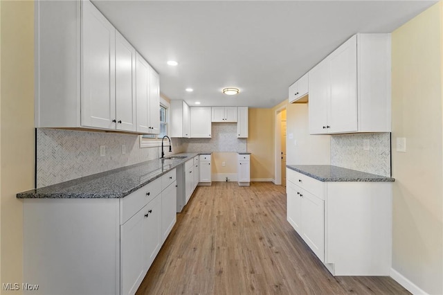 kitchen featuring dark stone counters, a sink, light wood-style floors, white cabinetry, and backsplash