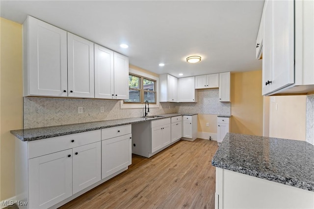 kitchen featuring light wood-style flooring, a sink, white cabinets, backsplash, and dark stone counters