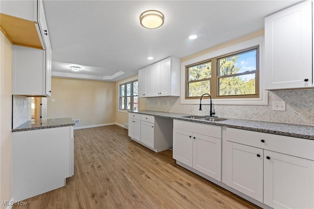 kitchen with light stone counters, a sink, white cabinets, decorative backsplash, and light wood finished floors