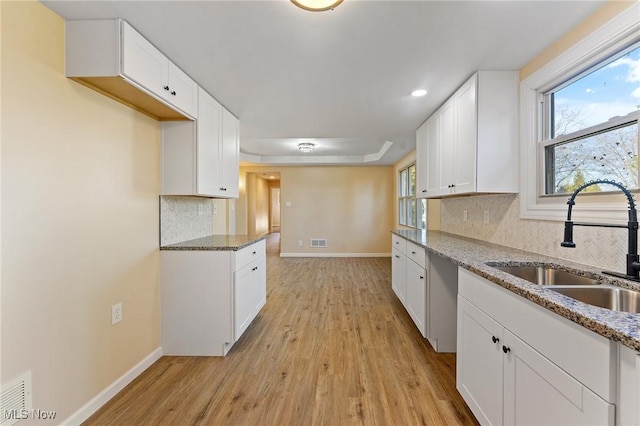 kitchen with white cabinets, light wood-style flooring, a sink, light stone countertops, and backsplash