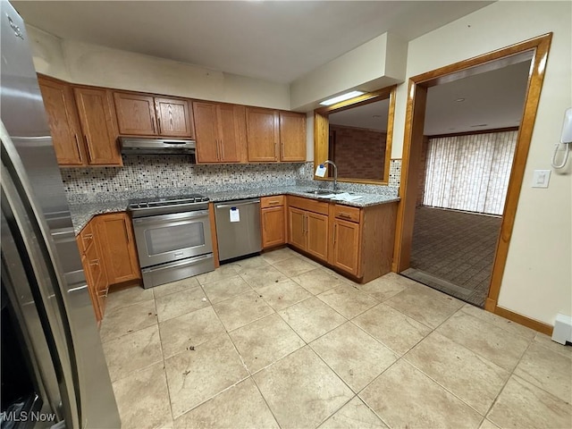 kitchen with under cabinet range hood, stainless steel appliances, a sink, decorative backsplash, and brown cabinetry