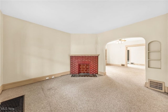 unfurnished living room featuring arched walkways, a fireplace, visible vents, carpet flooring, and baseboards