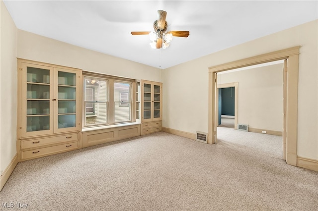 carpeted empty room with a ceiling fan, visible vents, and baseboards