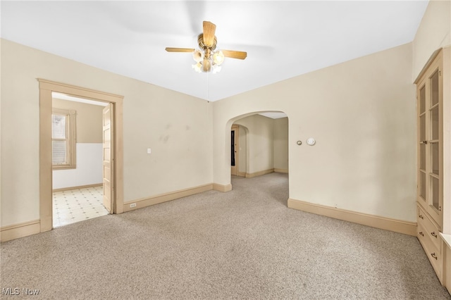 unfurnished room with arched walkways, baseboards, a ceiling fan, and light colored carpet