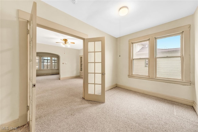 unfurnished room featuring carpet floors, arched walkways, french doors, a ceiling fan, and baseboards