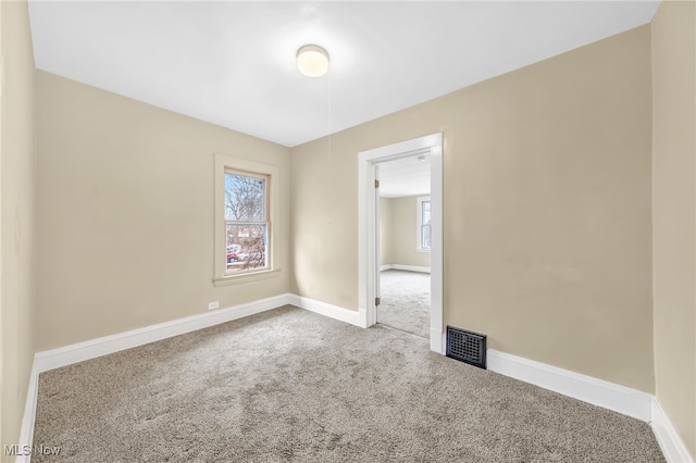 carpeted empty room featuring a wealth of natural light, visible vents, and baseboards