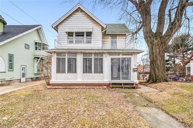 rear view of property featuring a shingled roof, a balcony, and a sunroom