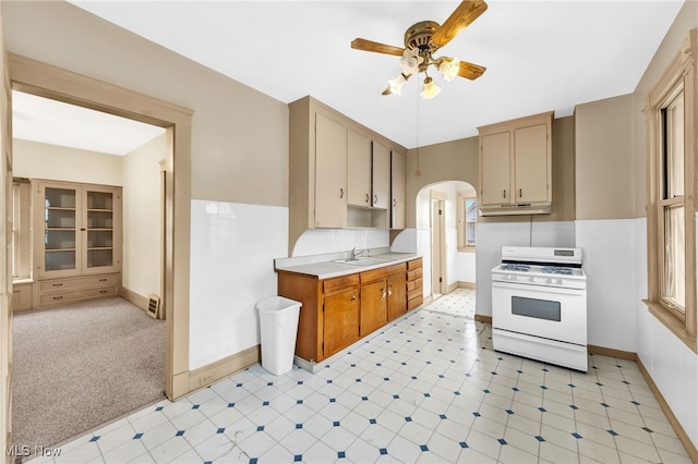 kitchen featuring arched walkways, white gas stove, light countertops, ceiling fan, and under cabinet range hood