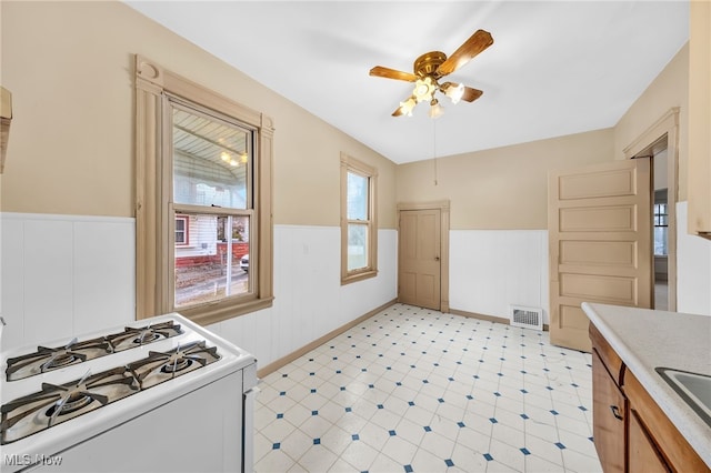 kitchen with a wainscoted wall, gas range gas stove, light floors, light countertops, and visible vents