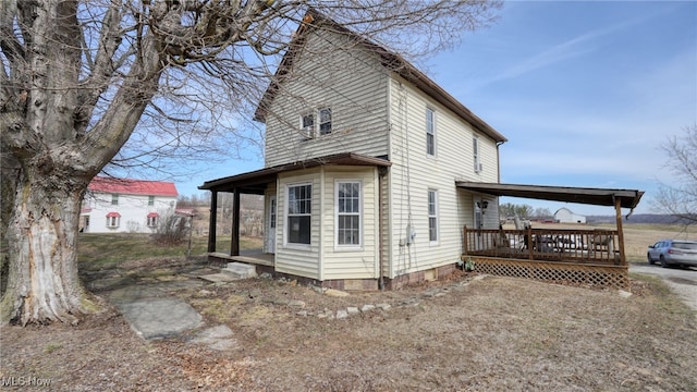 view of property exterior featuring an attached carport, a deck, and dirt driveway