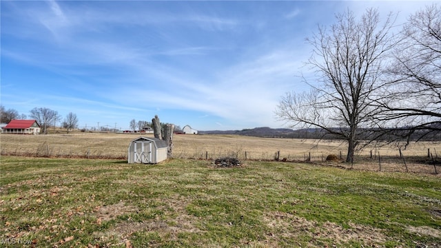 view of yard with a storage shed, a rural view, and fence