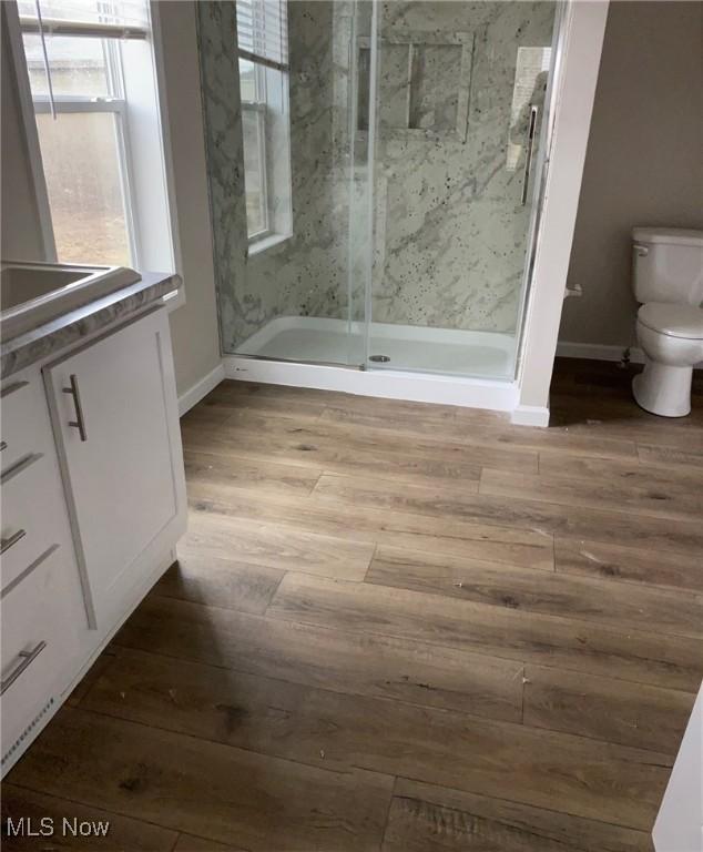 bathroom with a marble finish shower, wood finished floors, toilet, and baseboards