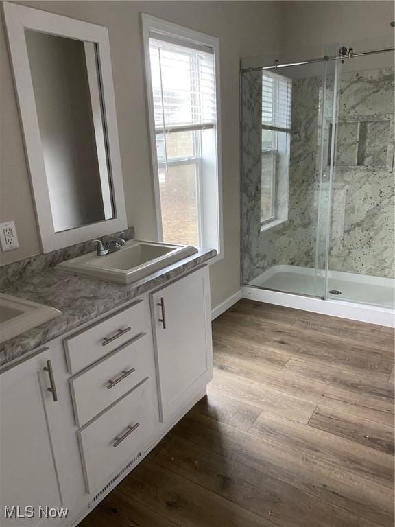 bathroom with double vanity, a sink, a marble finish shower, and wood finished floors