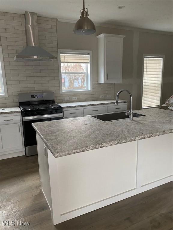 kitchen featuring dark wood-style flooring, a sink, gas range, wall chimney exhaust hood, and a center island with sink