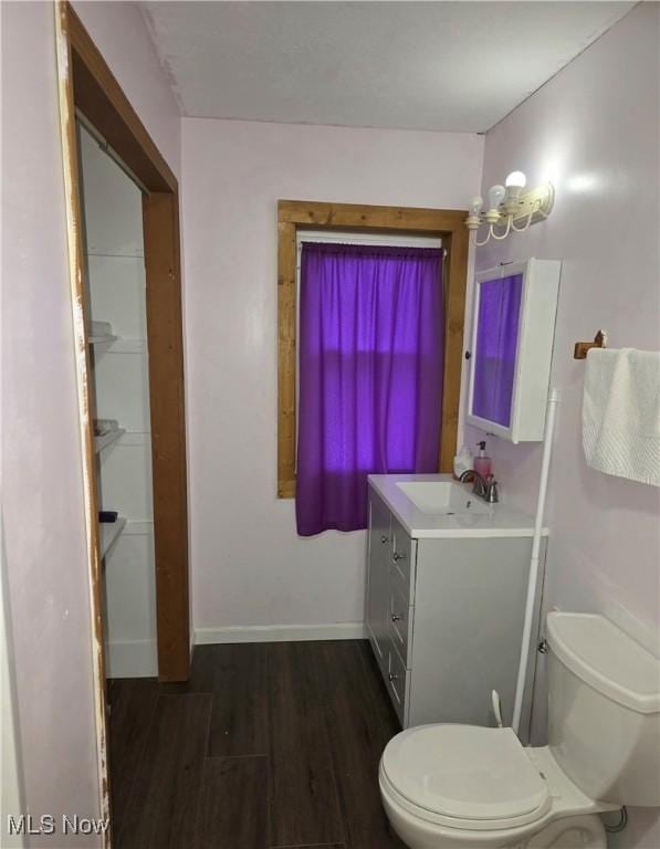 half bathroom with vanity, wood finished floors, toilet, and baseboards