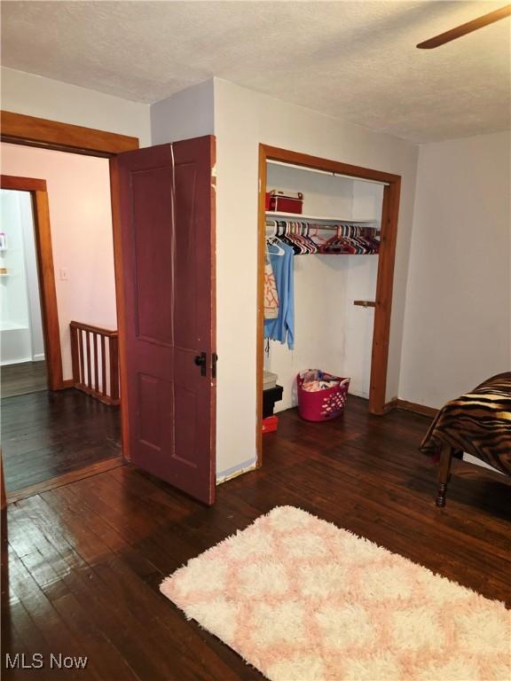 unfurnished bedroom with baseboards, ceiling fan, hardwood / wood-style floors, a textured ceiling, and a closet