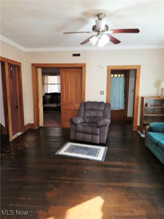 living area with wood finished floors, a ceiling fan, visible vents, baseboards, and ornamental molding