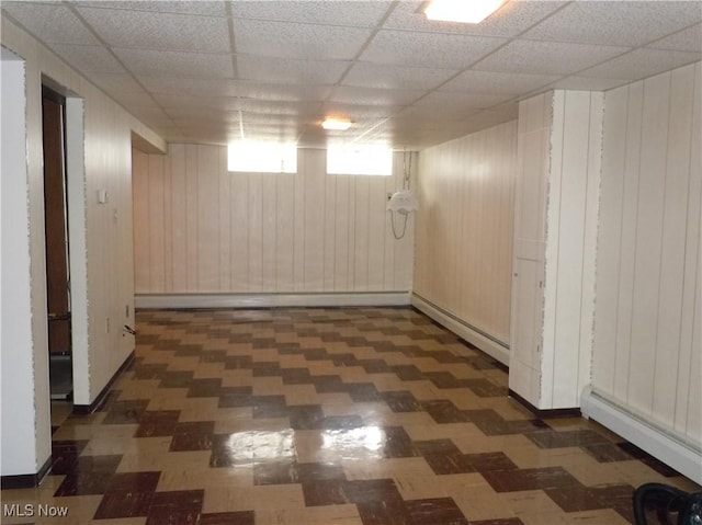 below grade area featuring a paneled ceiling, wood walls, and a baseboard heating unit