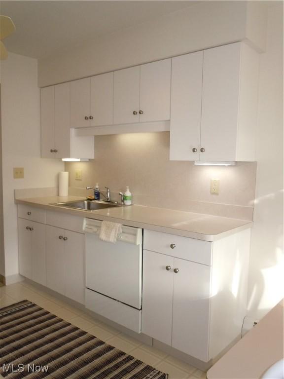 kitchen with light tile patterned floors, a sink, white cabinets, light countertops, and dishwasher