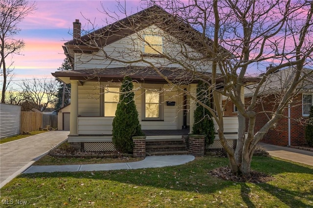 view of front facade with a chimney, covered porch, a lawn, fence, and driveway