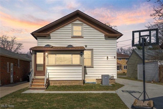 back of property at dusk featuring entry steps, a yard, and central air condition unit