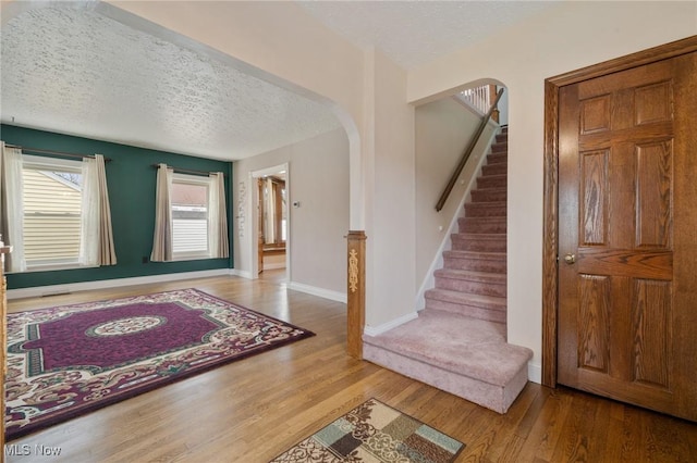 entrance foyer with arched walkways, a textured ceiling, wood finished floors, and stairs