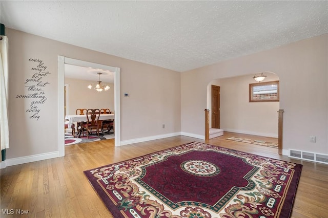 spare room featuring arched walkways, visible vents, a textured ceiling, wood finished floors, and baseboards