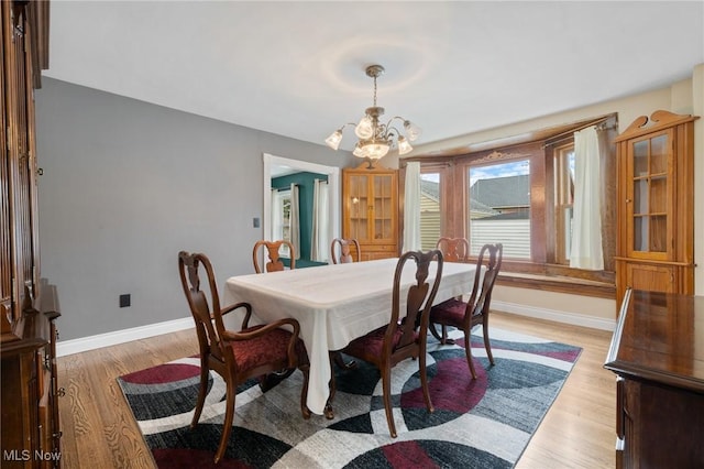 dining area with baseboards, light wood-type flooring, and a notable chandelier