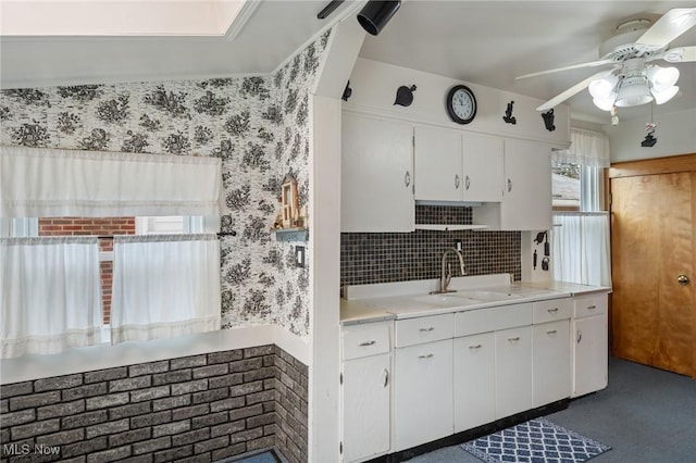 kitchen featuring wallpapered walls, a wainscoted wall, light countertops, white cabinetry, and a sink