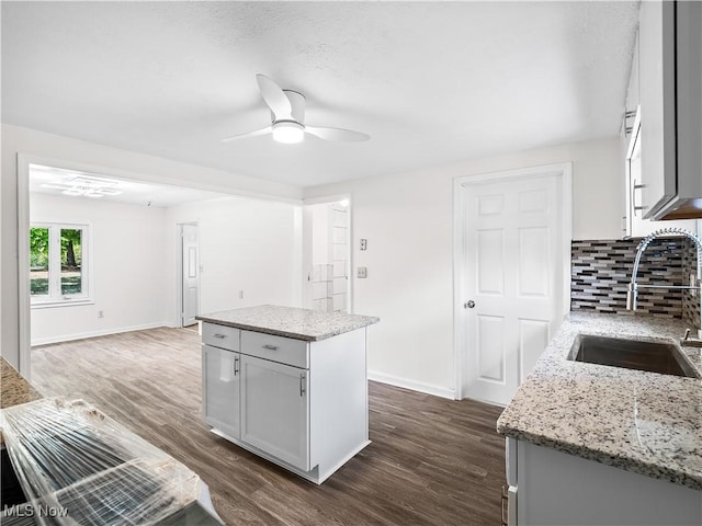 kitchen with tasteful backsplash, dark wood-type flooring, a sink, and light stone counters