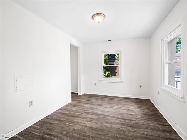 empty room featuring dark wood-style floors, plenty of natural light, and baseboards