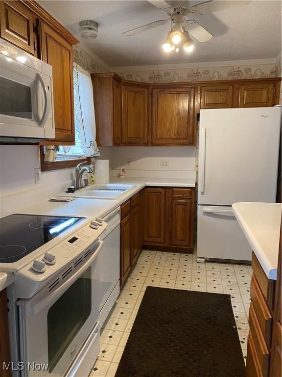 kitchen with white appliances, a sink, light countertops, light floors, and brown cabinetry