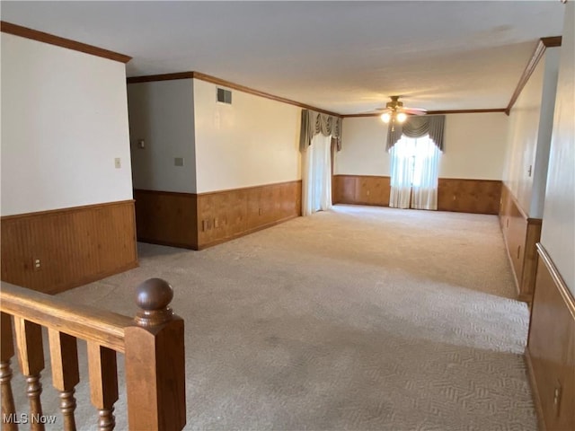 carpeted spare room featuring crown molding, visible vents, wainscoting, wood walls, and ceiling fan