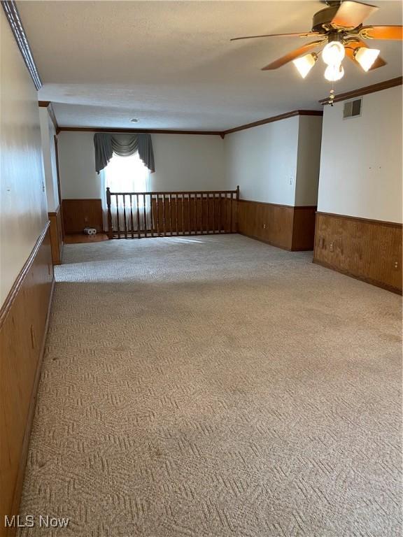 carpeted empty room featuring ornamental molding, wainscoting, visible vents, and wooden walls