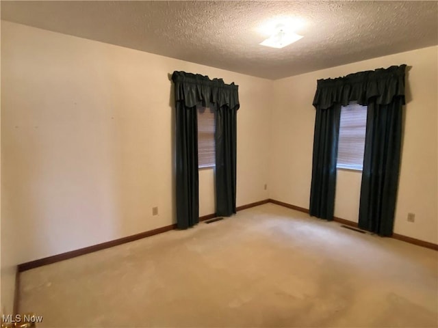 unfurnished room with baseboards, a textured ceiling, visible vents, and light colored carpet