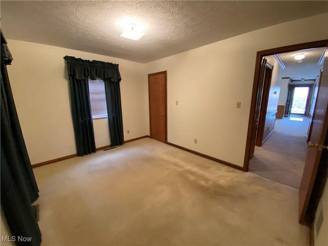 spare room with light colored carpet, a textured ceiling, and baseboards