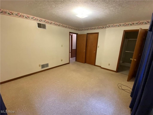 unfurnished bedroom featuring a textured ceiling, light colored carpet, visible vents, and baseboards